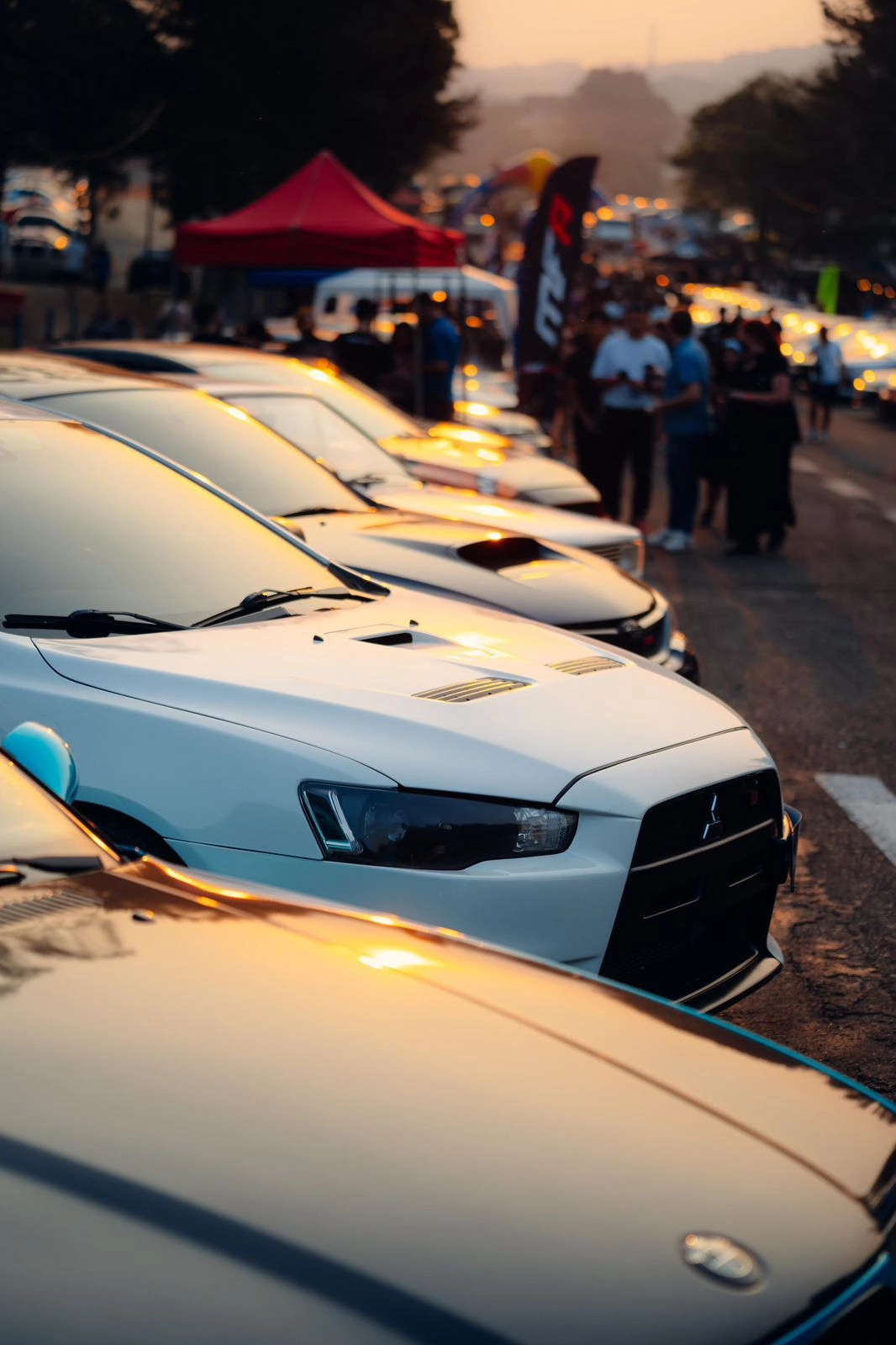 Mitsubishi Lancer branco estacionado em um encontro de carros ao entardecer