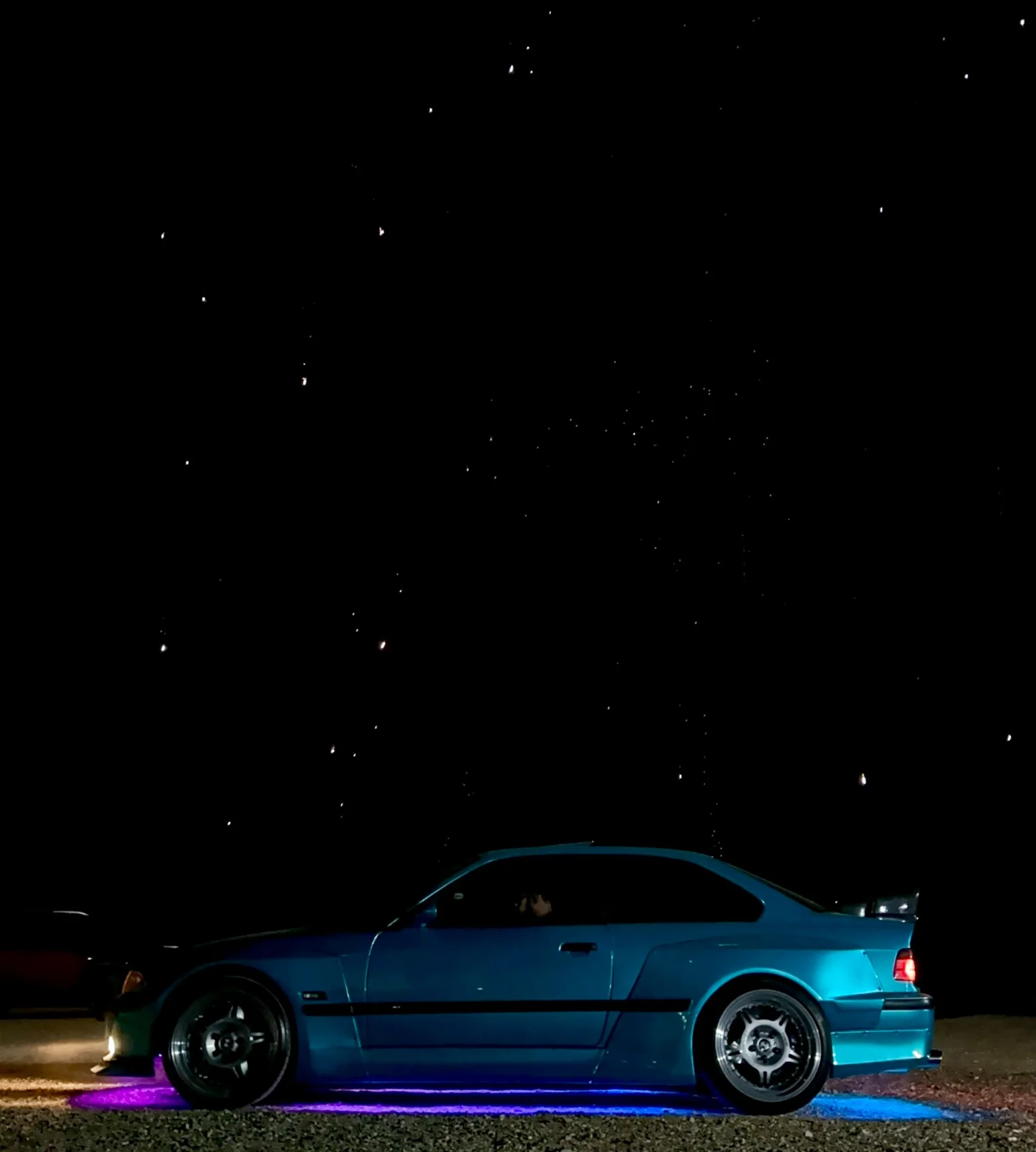 BMW E36 Sullivan de perfil à noite, com iluminação azul e roxa sob a carroceria